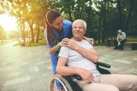 L'infirmière pose sa main sur l'épaule d'un homme en fauteuil roulant dans un parc