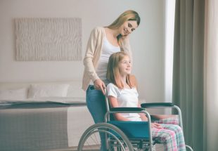 Une femme aide une adolescente en fauteuil roulant, toutes deux souriantes