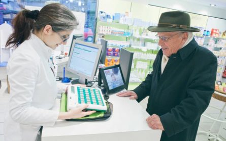 Une pharmacienne présente le pilulier Pharmagest à un homme âgé en pharmacie